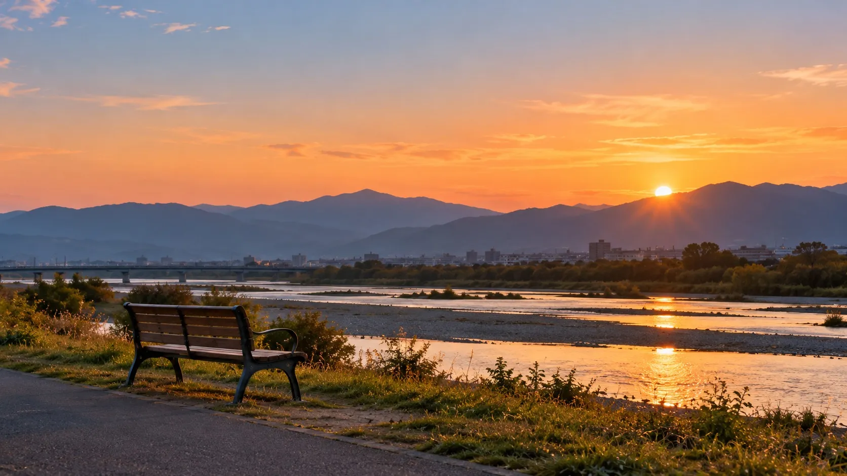 夕暮れの山並みと、河川敷の無人のベンチ